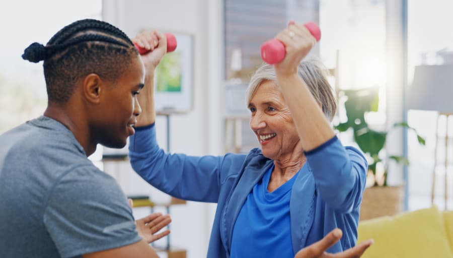 A man with outstretched hands assisting an elderly woman lifting hand weights