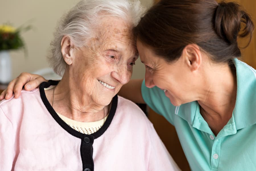 A senior woman and her caregiver touching foreheads and smiling