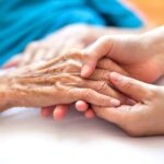 Close-up of a senior woman’s hand being held by a caregiver
